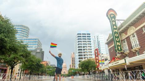 Man in faux cowboy hat waves rainbow flag on scooter in front of the Paramount Theater and Capitol Building Man in faux cowboy hat waves rainbow flag on scooter in front of the Paramount Theater and Capitol Building