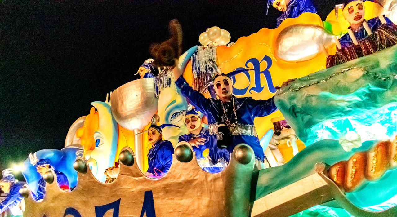Masked revelers entertain crowds at a nighttime Mardi Gras parade